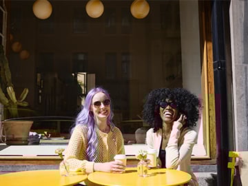 Två kvinnor sitter i solen på uteservering till café